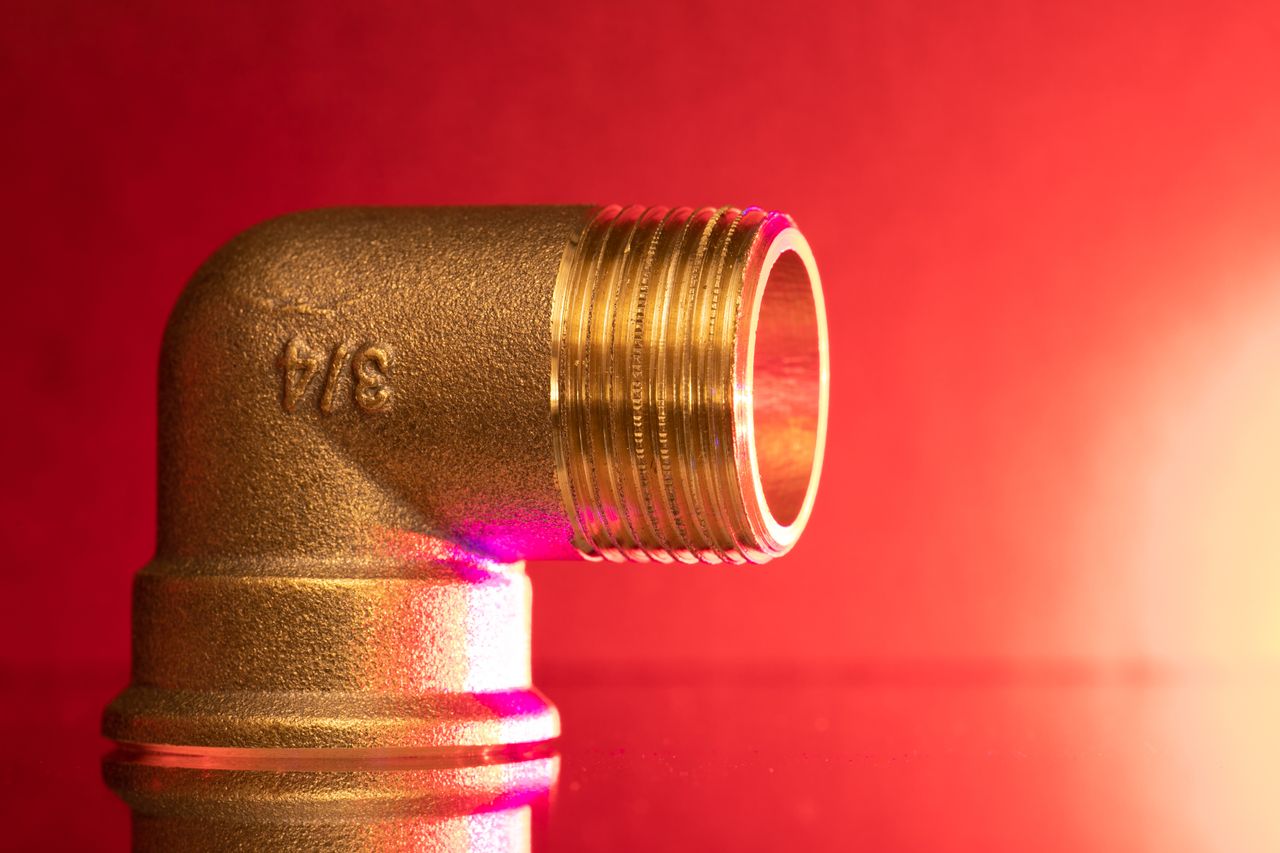 Services Close-up of a shiny brass pipe elbow fitting against a vibrant red backdrop, showcasing industrial elegance.